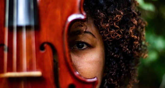 a violin covering up half the face of a person with brown skin and curly brown hair