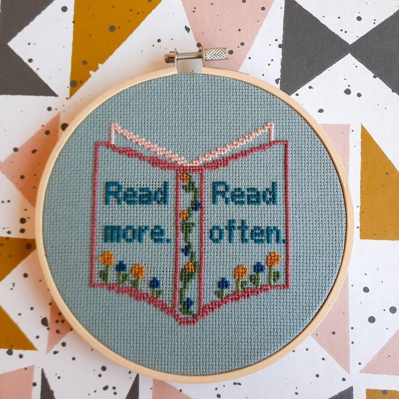 Image of a cross stitch. It's a book spine with the words "read more. read often." There are flowers on the book's spine. 