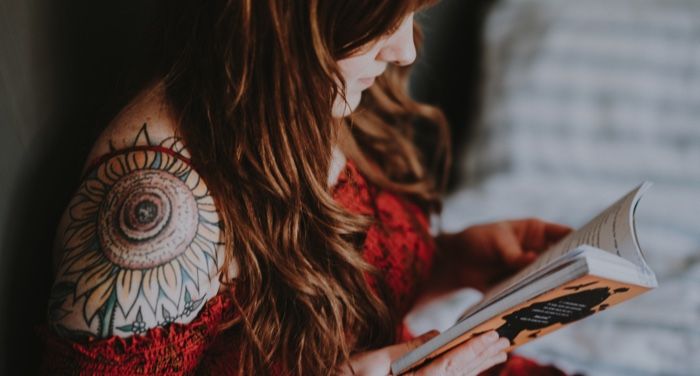 a person with red hair and white skin with tattoos reading a book