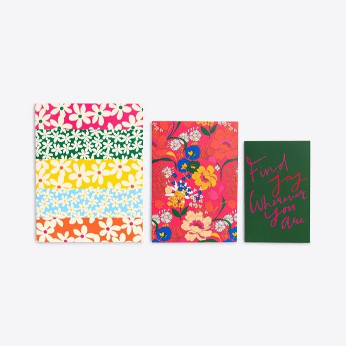 a set of three notebooks in ascending sizes; the larger two are floral themed, the small west is green with pink and red text that reads "find joy wherever you are"
