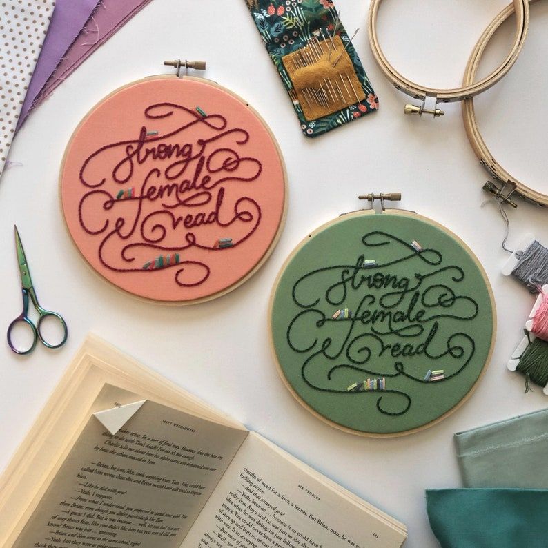 Two completed embroidery patterns reading "strong female read" in swirly letters. 