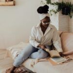 brown-skinned woman with kinky hair sits on a light tan couch reading