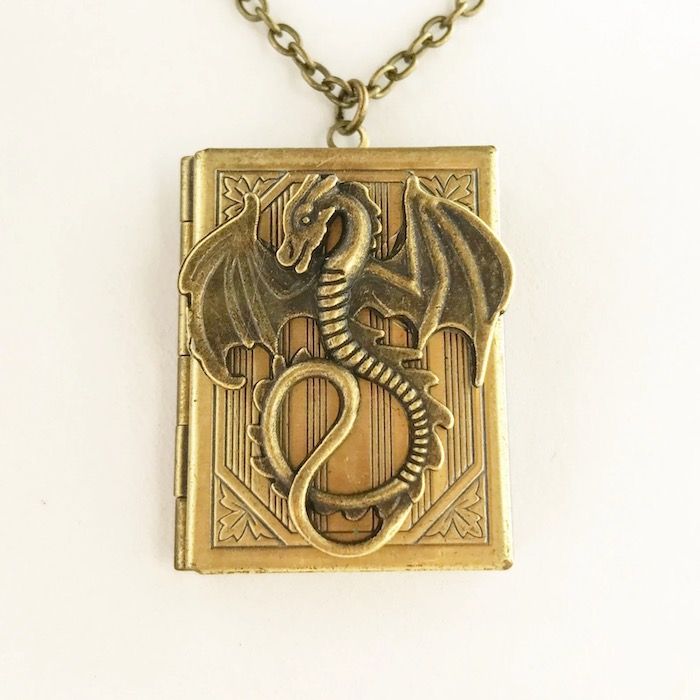 gold necklace with a book charm. The book is a locket with a dragon on the front