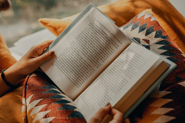 Hands holding an open book, resting on a southwestern print pillow