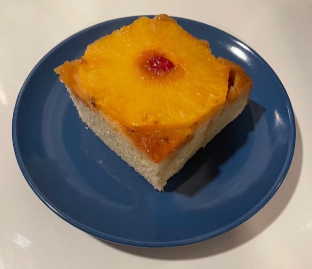 square piece of pineapple upside-down cake with a maraschino cherry on a blue plate