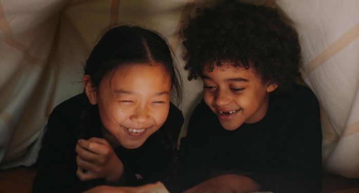 two kids with tan and light brown skin smiling under a blanket fort