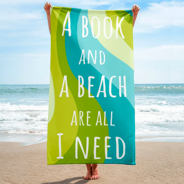 Person on a beach holding up a green and blue beach towel with text "A book and a beach are all I need"