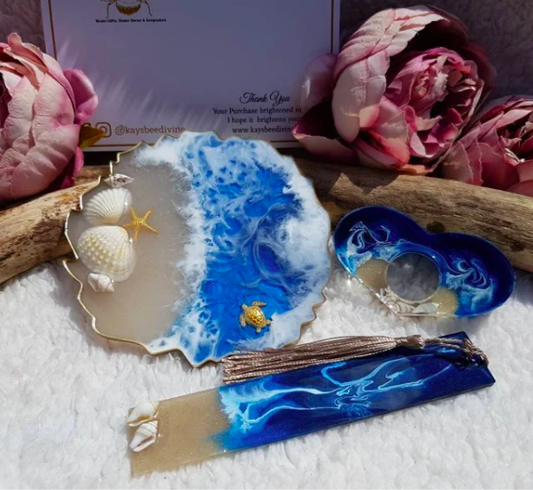 Set of three resin book accessories (bookmark, coaster, and page holder with hole for thumb) in blue and clear with seashells, on a white background with peonies