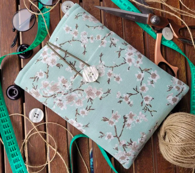 Fabric booksleeve with teal floral print and a button and tie, set on a wooden background