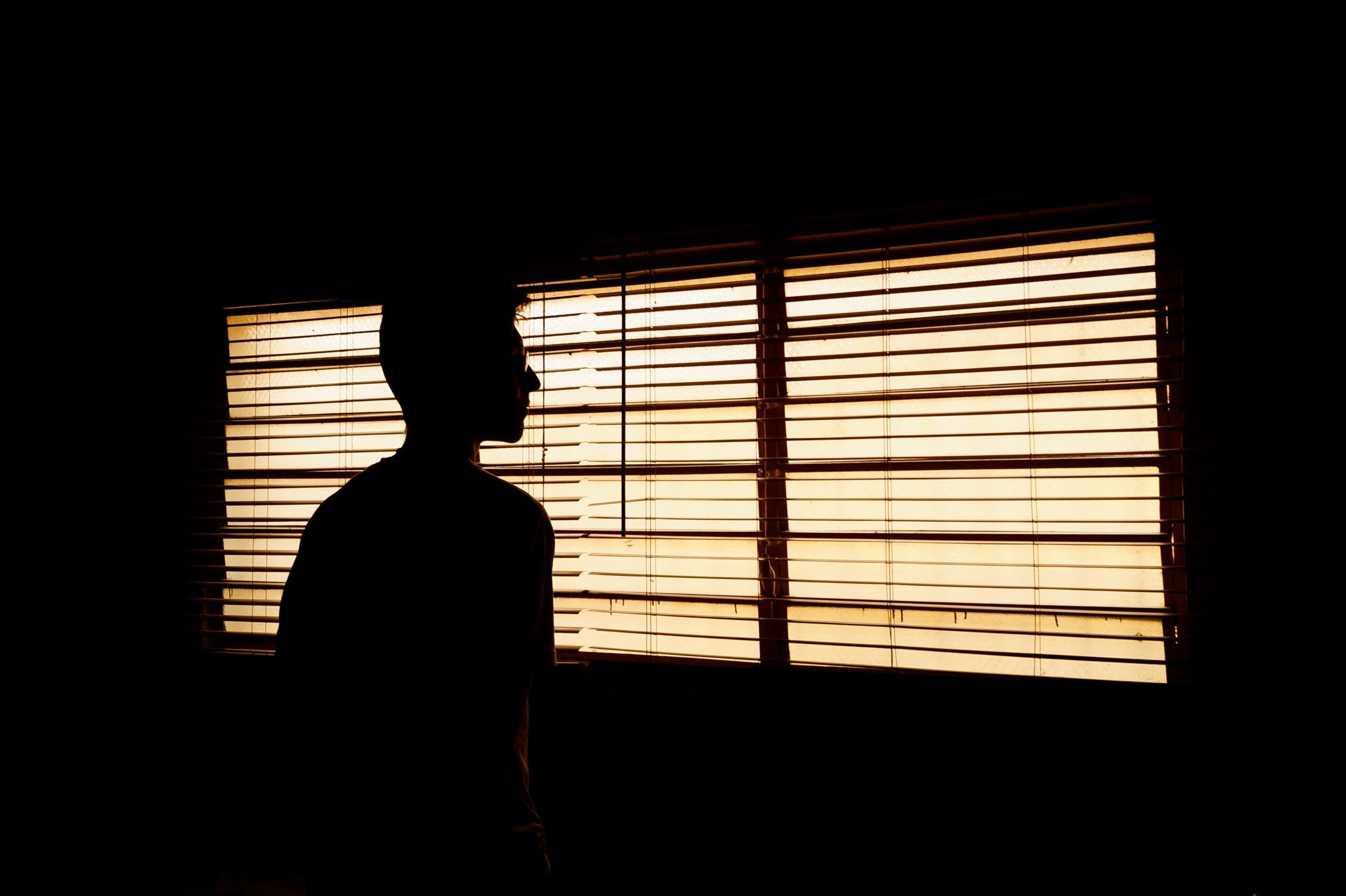 a person silhouetted against windows with blinds down