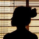 a photo of a woman silhouetted in a window with blinds