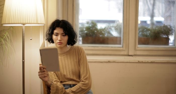 light-skinned woman with short, dark hair, a nose ring and sand-colored blouse reading