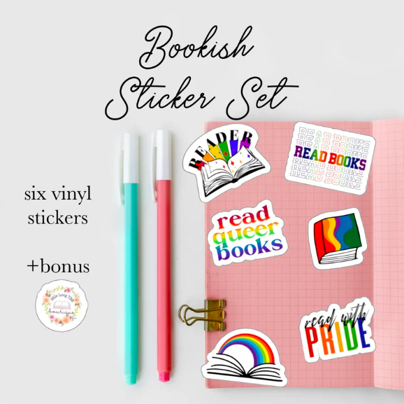 A set of six rainbow and queer books themed stickers, including one that says "read queer books", displayed next to a journal and pens