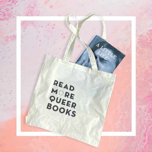 Tote bag that says "Read More Queer Books" with the book A Little Life partway out of the bag 