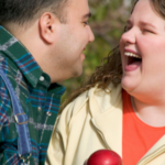a photo of a fat white man and woman laughing together in an apple orchard