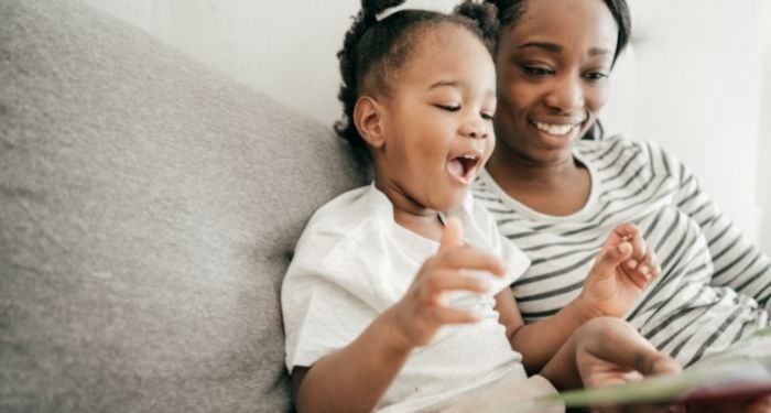 Image of a Black adult and Black child reading together on a couch.