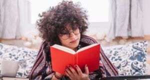 Image of an olive skinned person with curly hair reading a red book