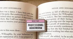 a photo of a small wooden pin that reads "Hello, I am a professional bookworm" resting on an open book