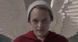 a still of Elisabeth Moss in the Handmaid's Tale with wings of a statue behind her