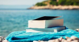 beach reads: a paperback on blue towel with a body of water in the background