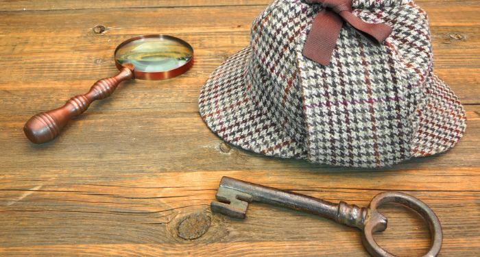 a deerstalker hat, an old key, and a magnifying glass on a wooden table