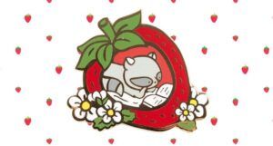 strawberry enamel pin with a raccoon reading inside