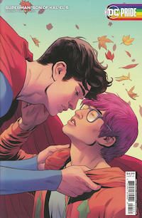 The cover of Superman: Son of Kal-El #5. Jon, in costume and in flight, is bending to kiss Jay, a young man with magenta hair and glasses. The cover has a rainbow DC Pride logo.