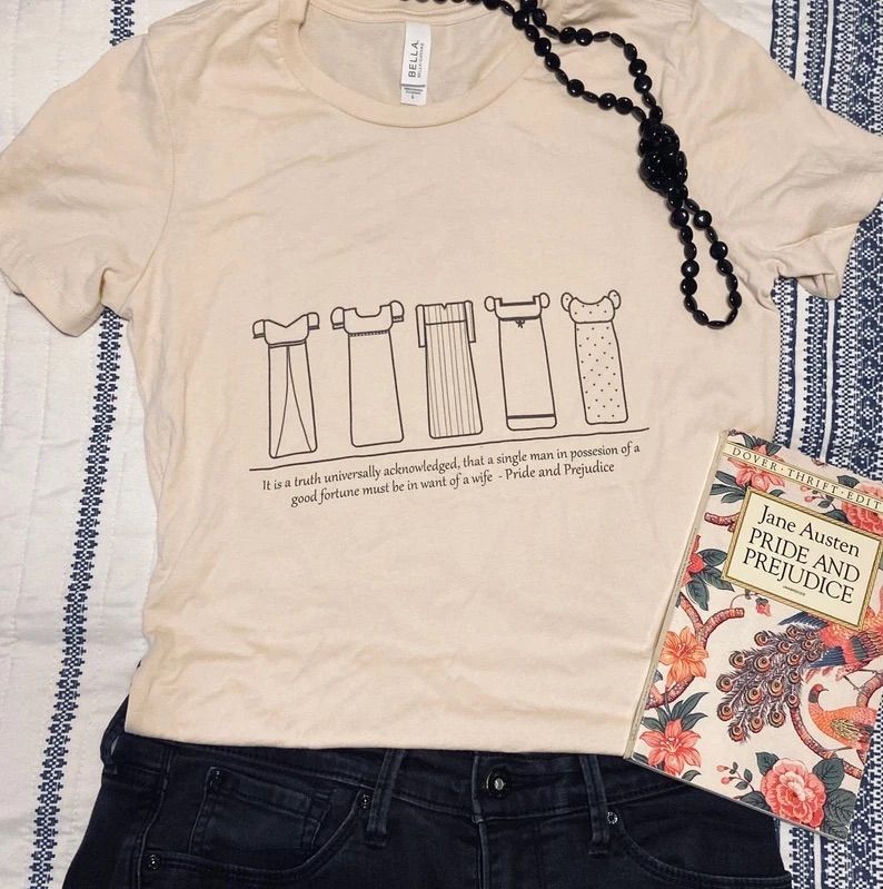 Photo of a t-shirt showing the dresses of each of the sisters in Pride And prejudice with the opening line of the book printed underneath. 