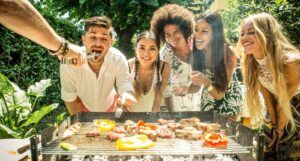 five men and women of various skin tones smiling behind a grill with food on it