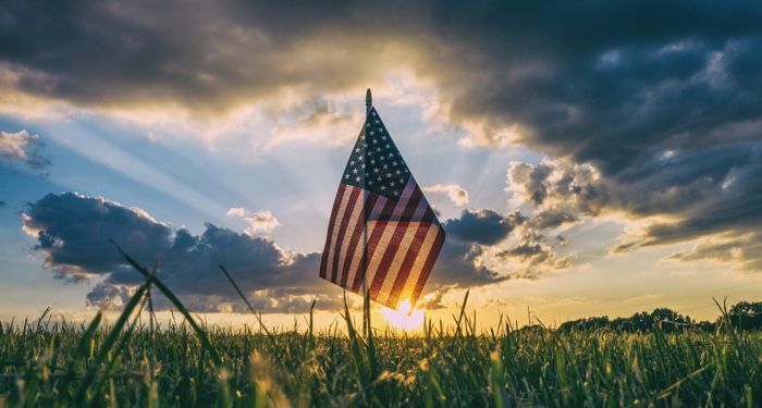 an American flag in a field of grass at sunrise
