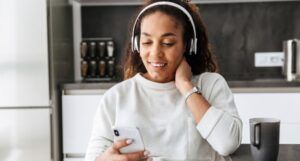 woman with brown skin wearing a set of white headphones and holding a cell phone in one hand