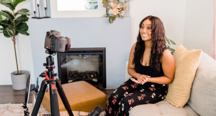 a woman with brown skin filming a video in a living room