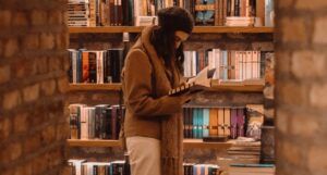 long-haired, light-skinned person reading book in bookstore