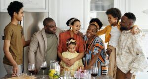 a photo of a large Black family hugging and laughing around a table with glasses