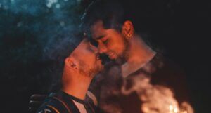 two lightly tanned-skin men nuzzle each other by sparklers