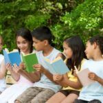 kids with skin tones ranging from light to tan sit on a bench with books
