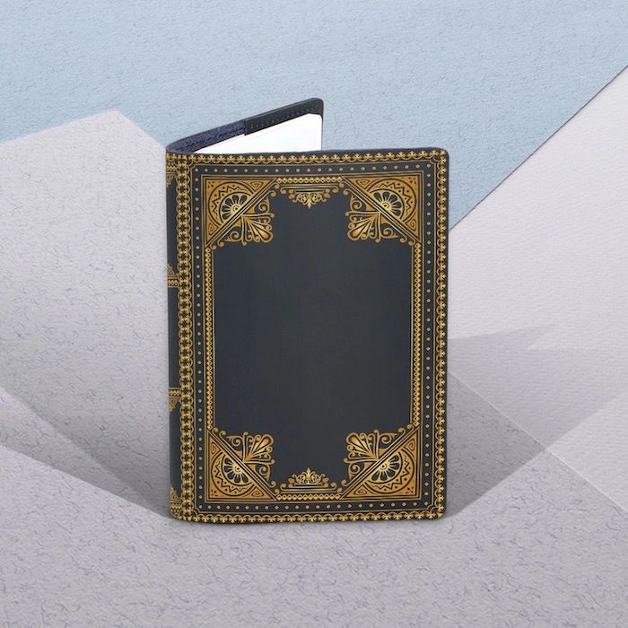 a passport cover that resembles a vintage book with a dark grey cover and gold edge detailing