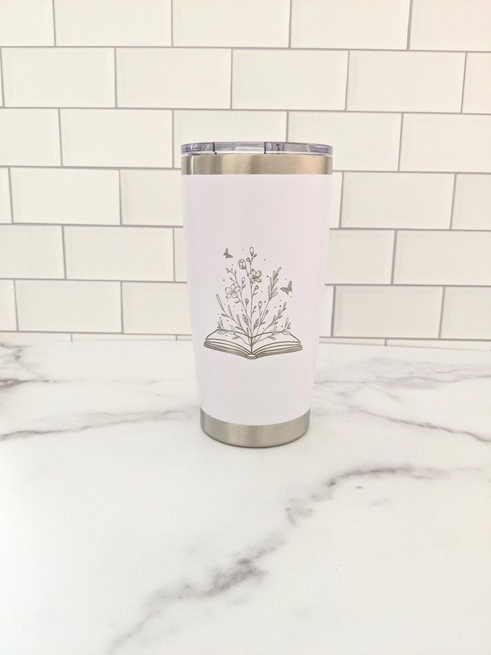 a white and silver tumbler with a design of flowers growing out of an open book 