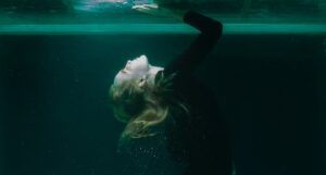 a photo of a woman underwater, holding her hand up against the glass above her