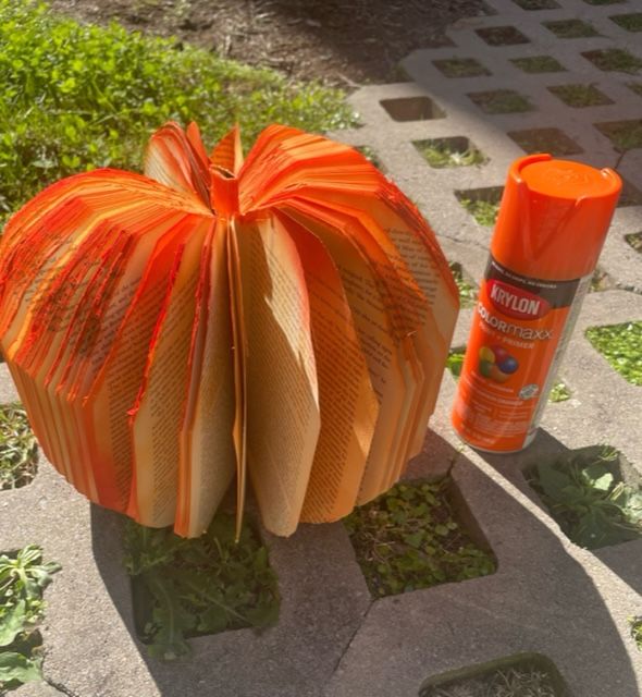 Book pumpkin is sitting on concrete lattice outside and has been spray painted orange around the edges. Next to it is the spray paint can.