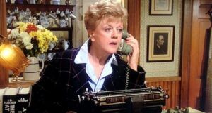 a still from Murder She Wrote showing Angela Lansbury at a typewriter, talking on the phone