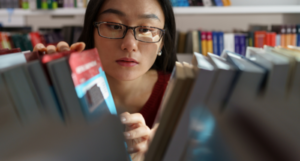 a photo of a young Asian woman looking through books on a library shelf