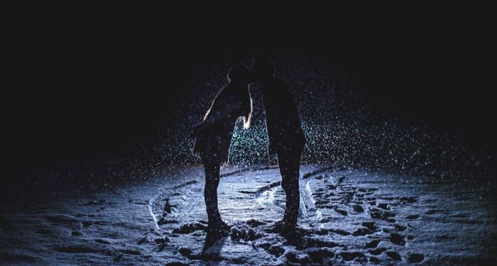 a couple kissing in the snow backlit by moonlight