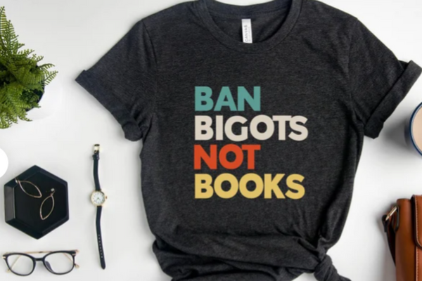 Dark heather gray short sleeved tee-shirt reading in all caps "BAN BIGOTS NOT BOOKS" in teal, white, red, and yellow respectively.