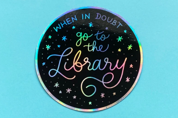 Black sticker with rainbow holographic text reading "When in doubt, go to the library" in cursive.