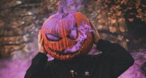 a photo of someone wearing a jack o lantern head with purple smoke billowing out of it