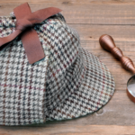 a photo of a magnifying glass and sherlock hat on a wood table
