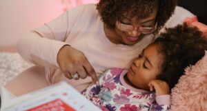 Black woman and young Black girl reading on a pink bed