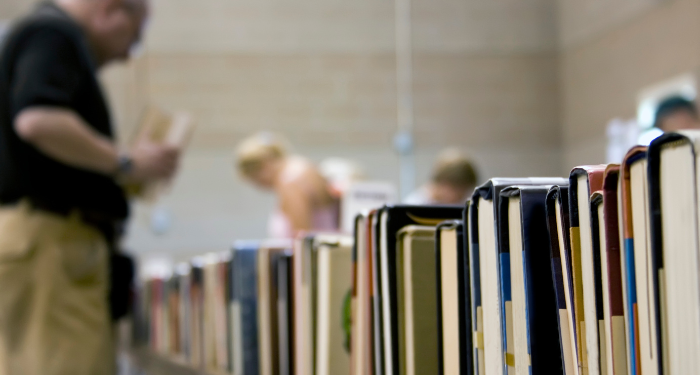 a photo taken at a used book sale of books on a table with blurred people on the background