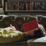 a photo of a woman lying on a couch with a book over her face